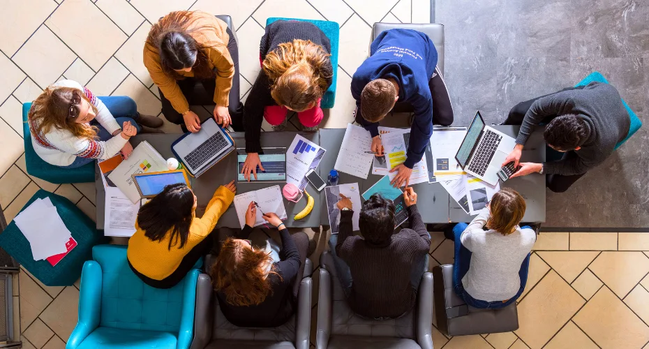 Several individuals seated at a table, focused on their laptops while engaging in a collaborative work session.