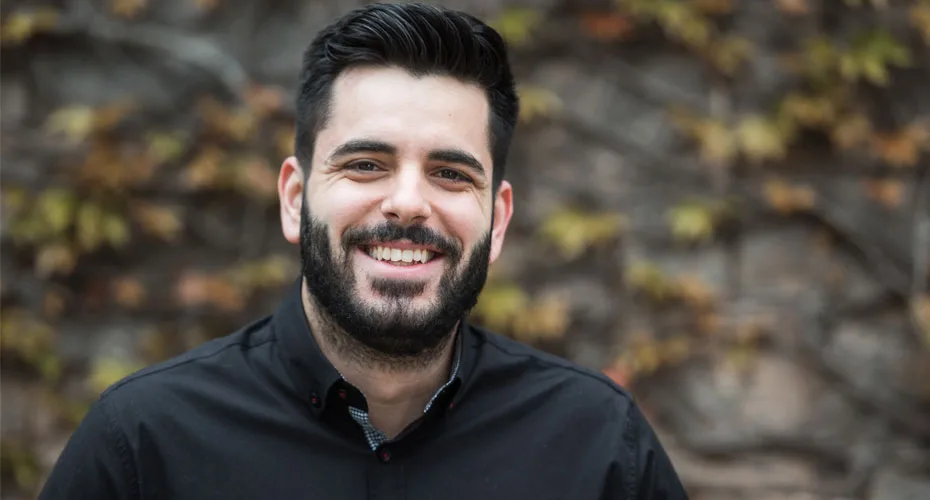 A smiling man with a beard in a black shirt, representing a master's business student.