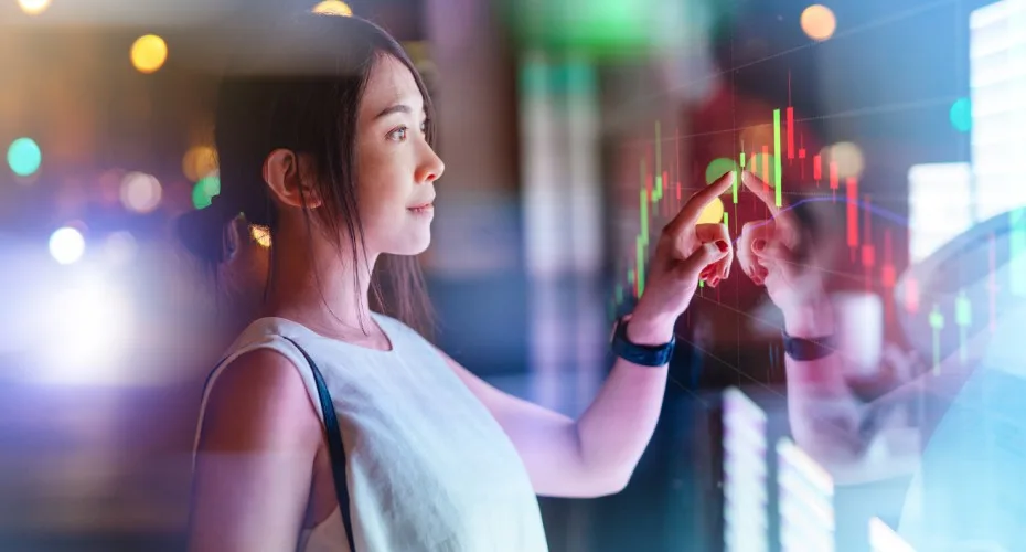 Young Asian businesswoman analysing investment data, touching on digital display.