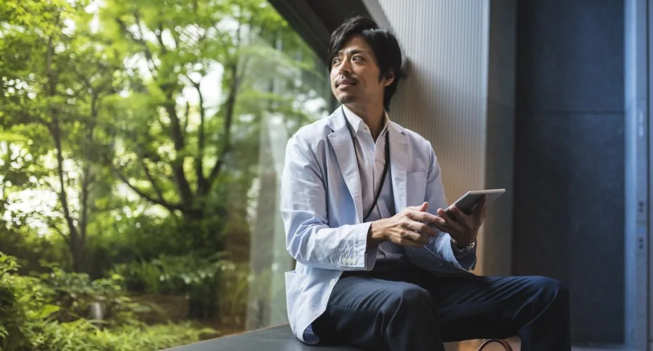 A Japanese businessman working on a project using digital tablet and looking outside the window. Photo by PAzmanJaka.