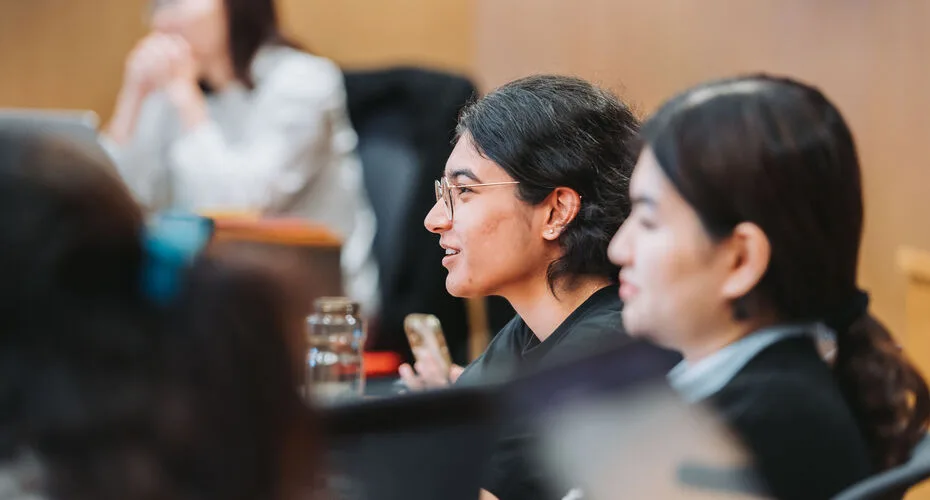 A group of MBA students engaged in discussion around a conference table during a lecture.