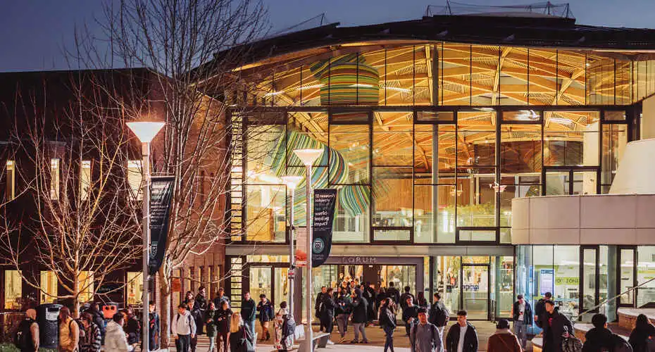 People walking outside the Forum building at night on Streatham Campus, with a lively and busy atmosphere.